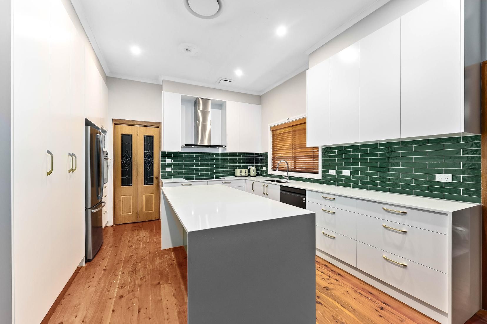Modern Kitchen with White Cabinets, Green Backsplash, Island, and Wooden Floors — Above & Beyond Interiors Custom Joinery in Minto, NSW