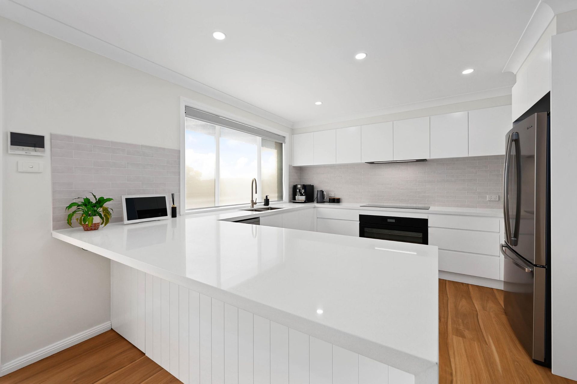 Modern White Kitchen with Island, Stainless Steel Appliances, and Light Wood Flooring — Above & Beyond Interiors Custom Joinery in Mount Anna, NSW