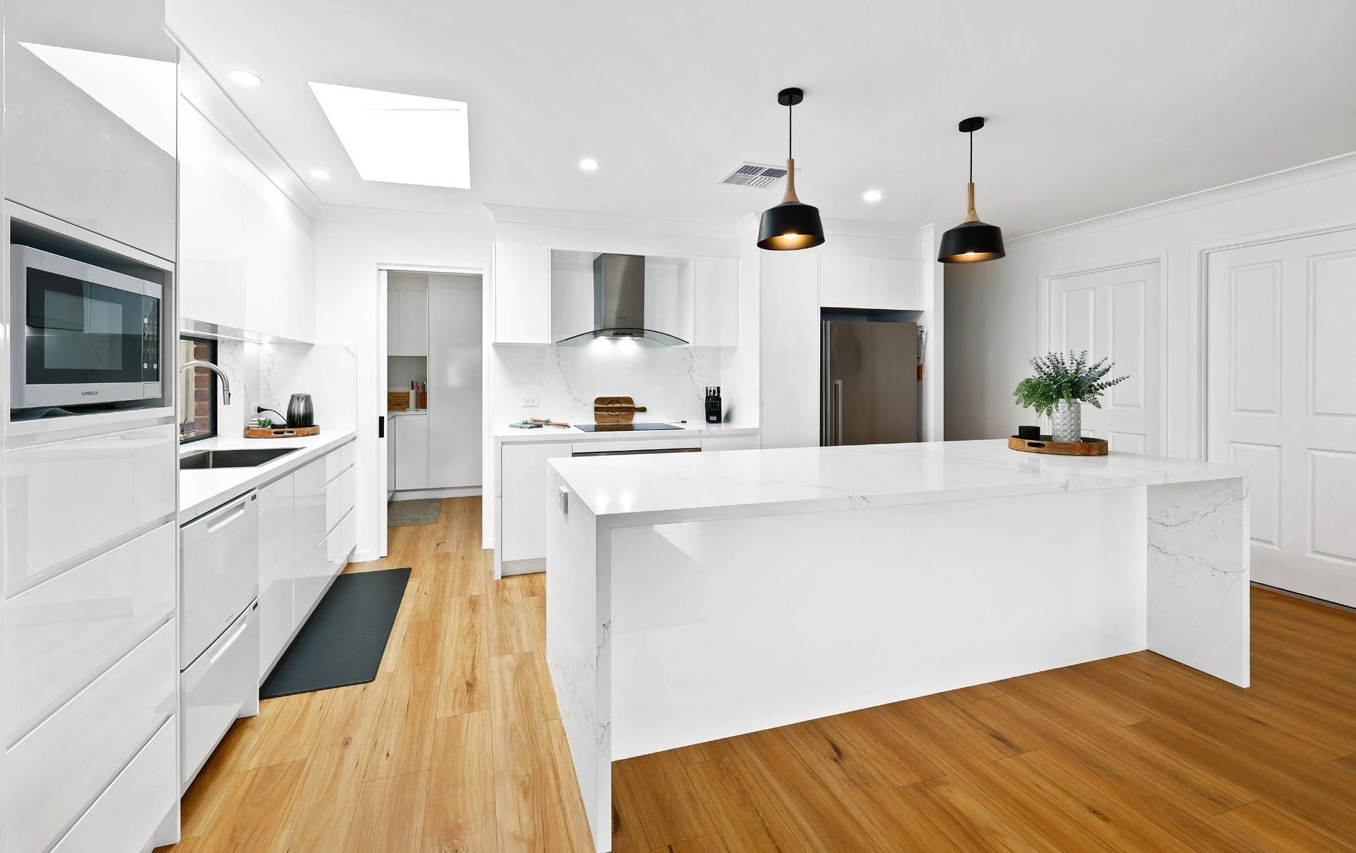 Modern White Kitchen with Hardwood Floors, Large Island, and Pendant Lights — Above & Beyond Interiors Custom Joinery in Wattle Grove, NSW