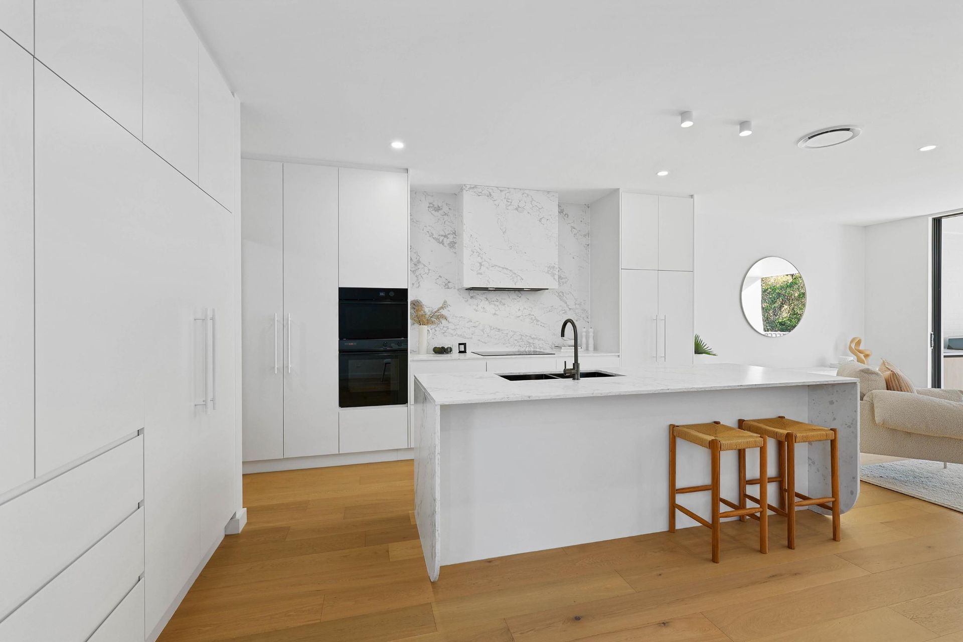 Modern All-White Kitchen with Island, Wooden Stools, and Marble Backsplash, and Wooden Floors — Above & Beyond Interiors Custom Joinery in Thirroul, NSW