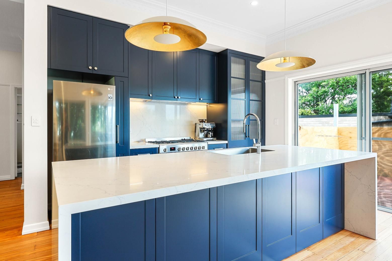 Modern Navy Blue Kitchen with Island, White Countertop, Gold Pendant Lights, and Stainless Steel Appliances — Above & Beyond Interiors Custom Joinery in Lilyfield, NSW