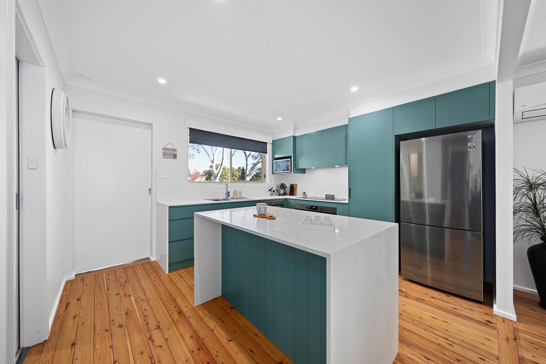 Kitchen with Teal Cabinets, White Countertops, Island, Wood Floor, and Stainless Steel Refrigerator — Above & Beyond Interiors Custom Joinery in Bradbury, NSW