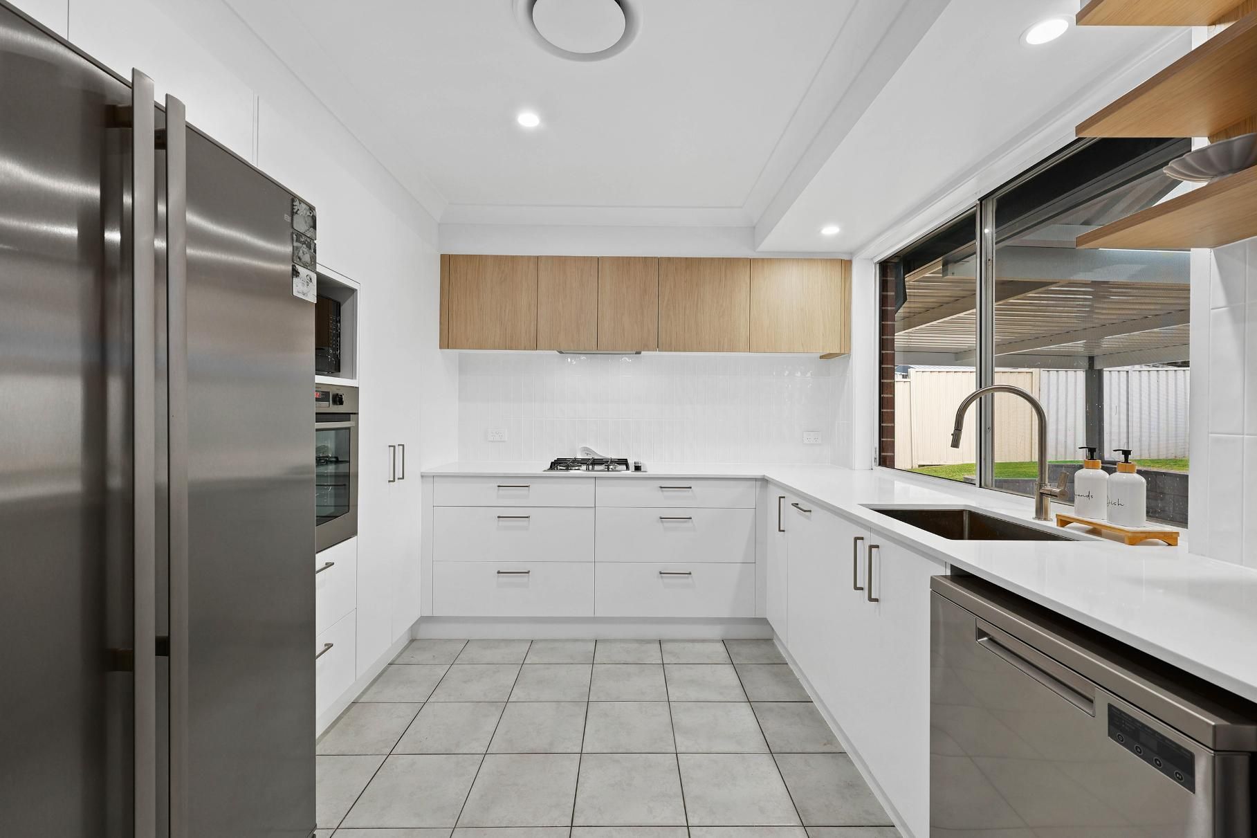 Modern White Kitchen with Stainless Steel Appliances, Light Wood Cabinets, and A View to The Backyard — Above & Beyond Interiors Custom Joinery in Currans Hill, NSW