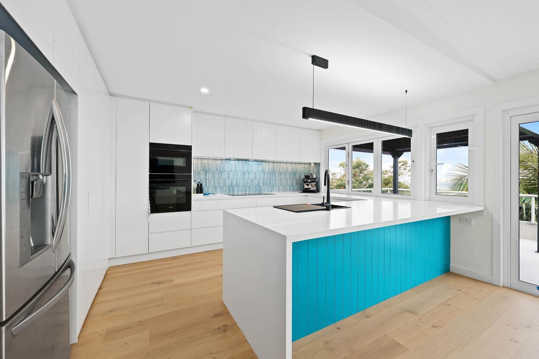 Modern White Kitchen with Turquoise Island, Stainless Steel Appliances, and Light Wood Floors — Above & Beyond Interiors Custom Joinery in North Curl Curl, NSW