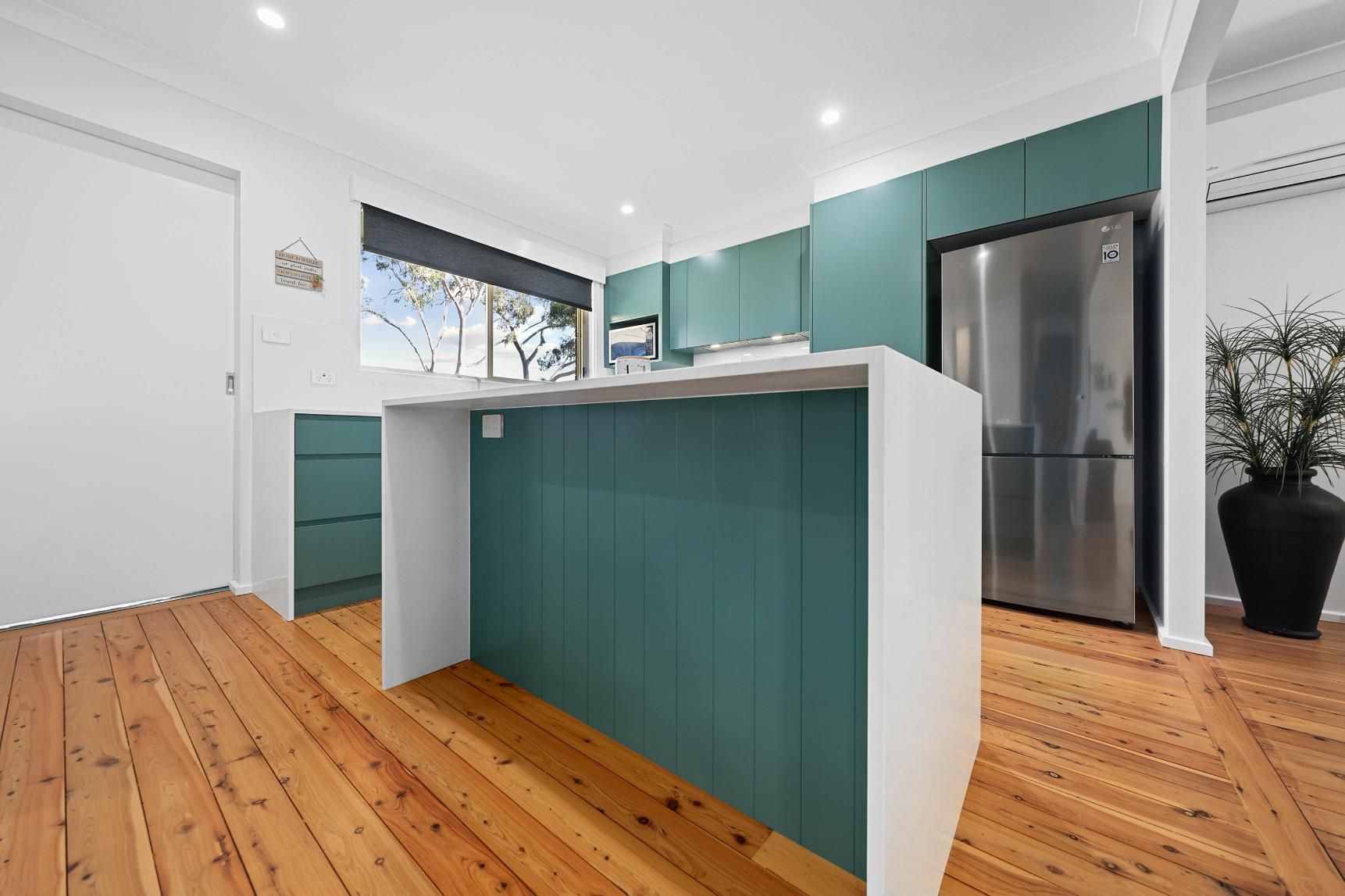 Modern Kitchen with Teal Cabinets and White Island, Stainless Steel Refrigerator, and Wood Flooring — Above & Beyond Interiors Custom Joinery in Bradbury, NSW