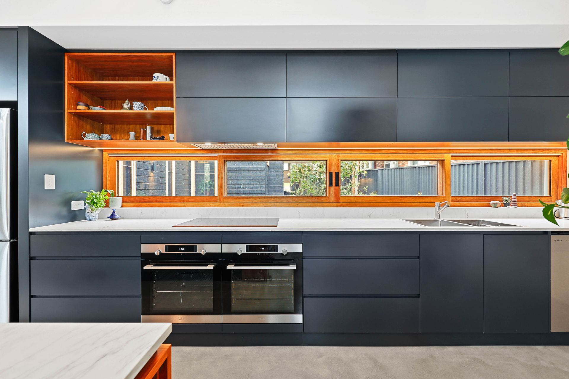 Modern kitchen with navy cabinets, wood-framed window, stainless steel appliances, and white countertop — Above & Beyond Interiors Custom Joinery in Bellambi, NSW