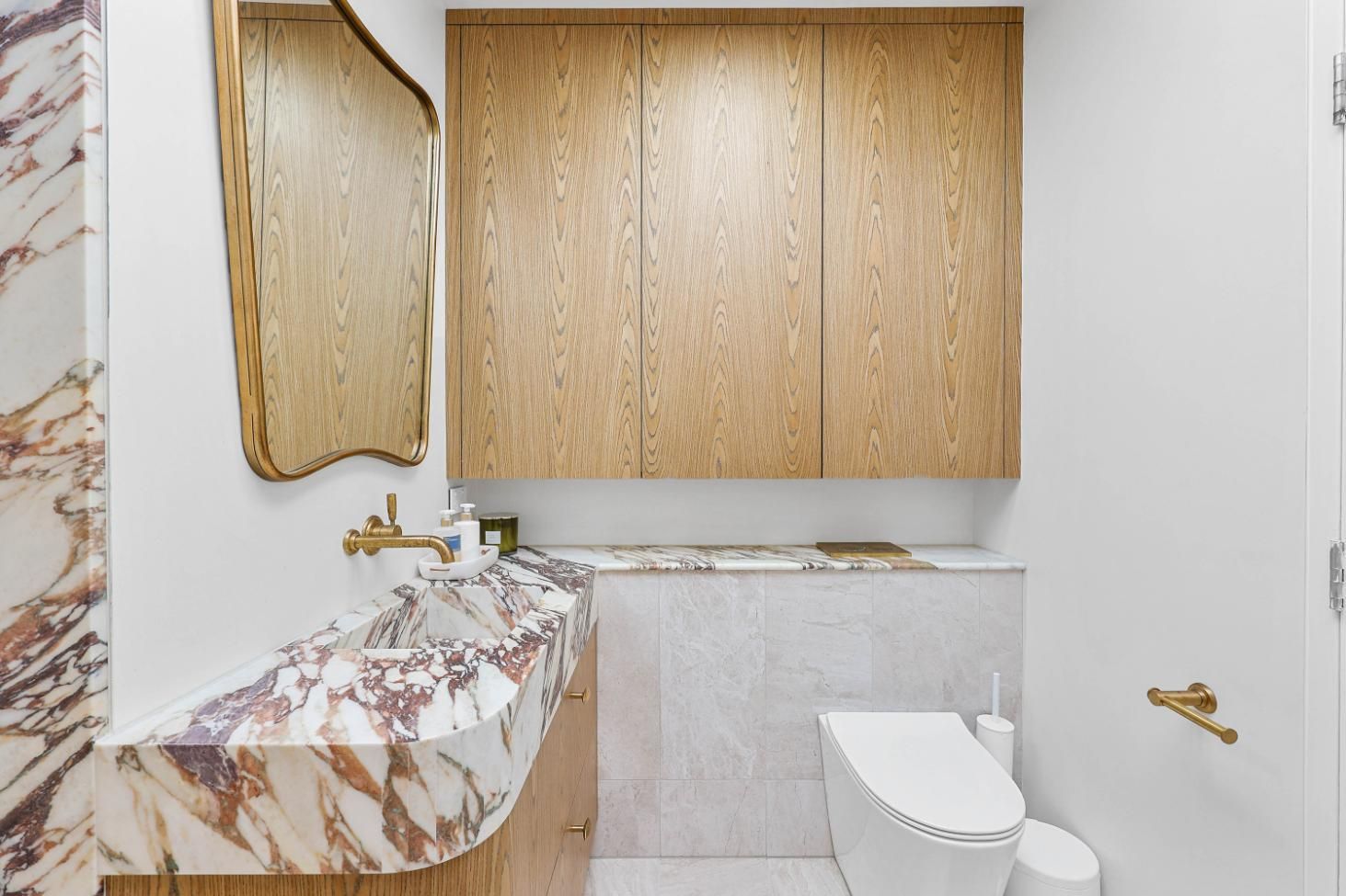 Powder Room: Marble Sink and Backsplash, Wood Cabinets, Gold Mirror and Fixtures, White Toilet — Above & Beyond Interiors Custom Joinery in Double Bay, NSW