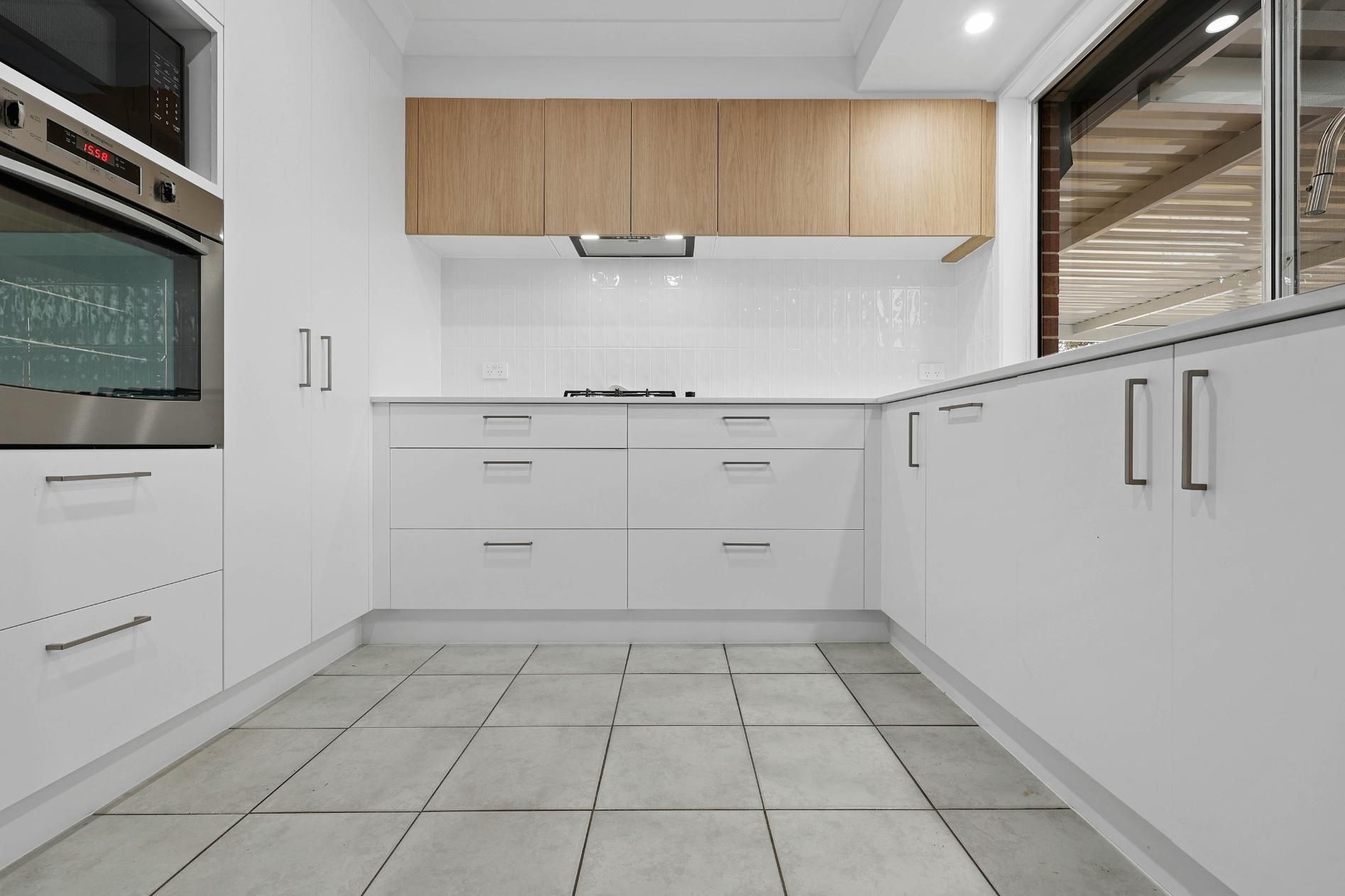 Modern White Kitchen with Wood-Tone Upper Cabinets, Stainless Steel Oven, and Grey Tiled Floor — Above & Beyond Interiors Custom Joinery in Currans Hill, NSW