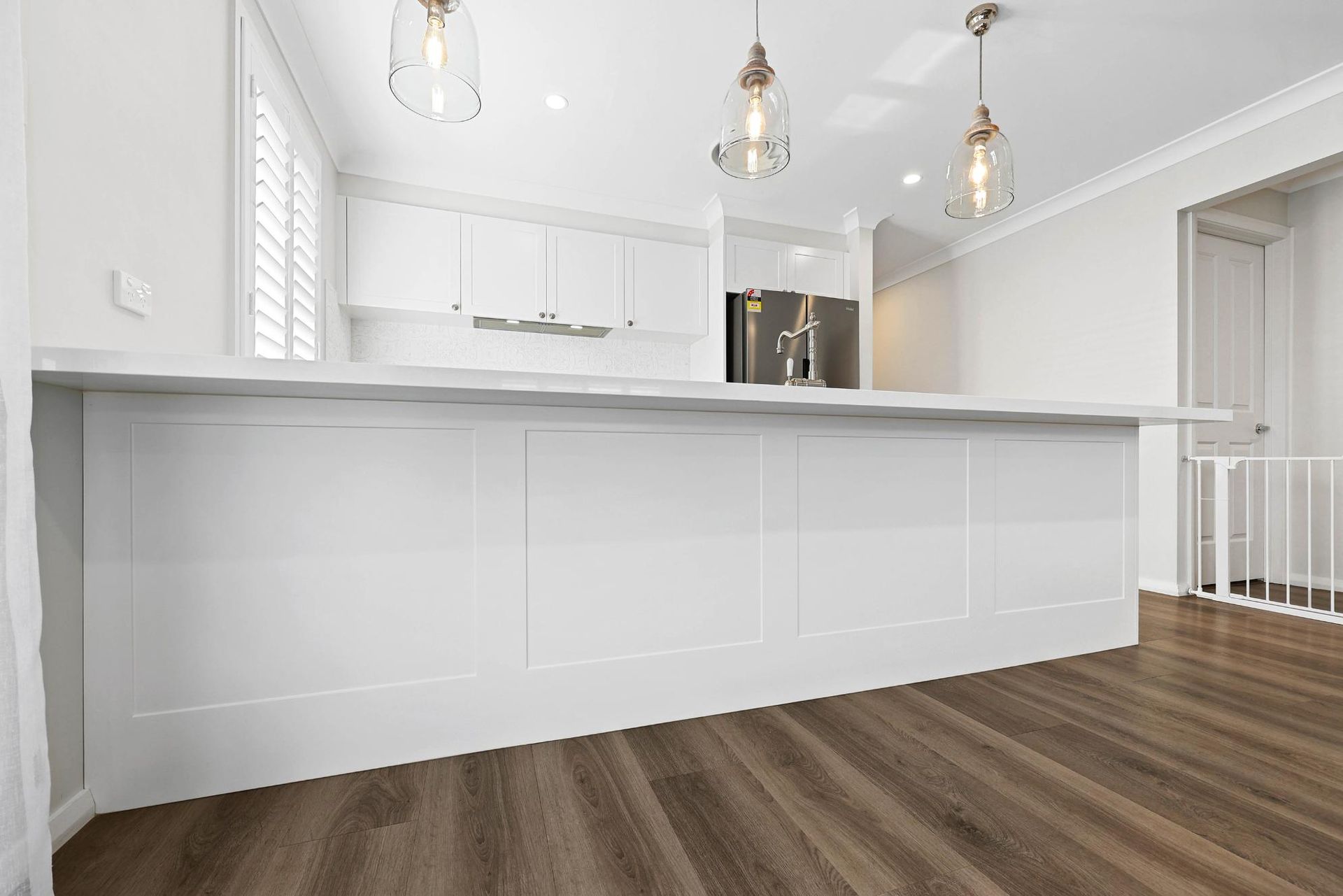 White Kitchen with Island, Wood Floors, Pendant Lights, and Stainless Steel Appliances — Above & Beyond Interiors Custom Joinery in Thirlmere, NSW
