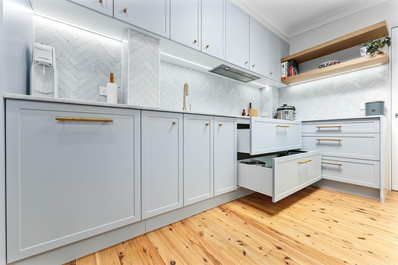 Light Blue Kitchen with Gold Hardware, Light Wooden Floors, and Open Drawers — Above & Beyond Interiors Custom Joinery in Erskineville, NSW