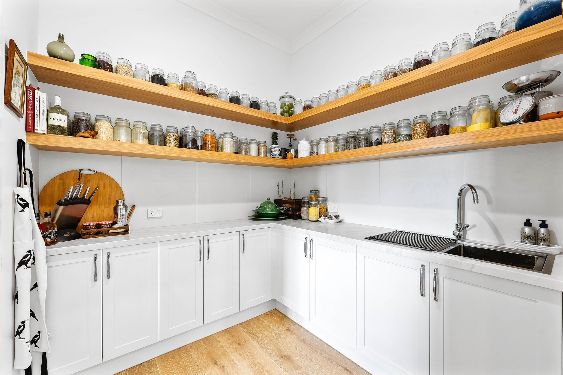 Bright white pantry with wooden shelves filled with jars, white cabinets, and a sink — Above & Beyond Interiors Custom Joinery in Bradbury, NSW
