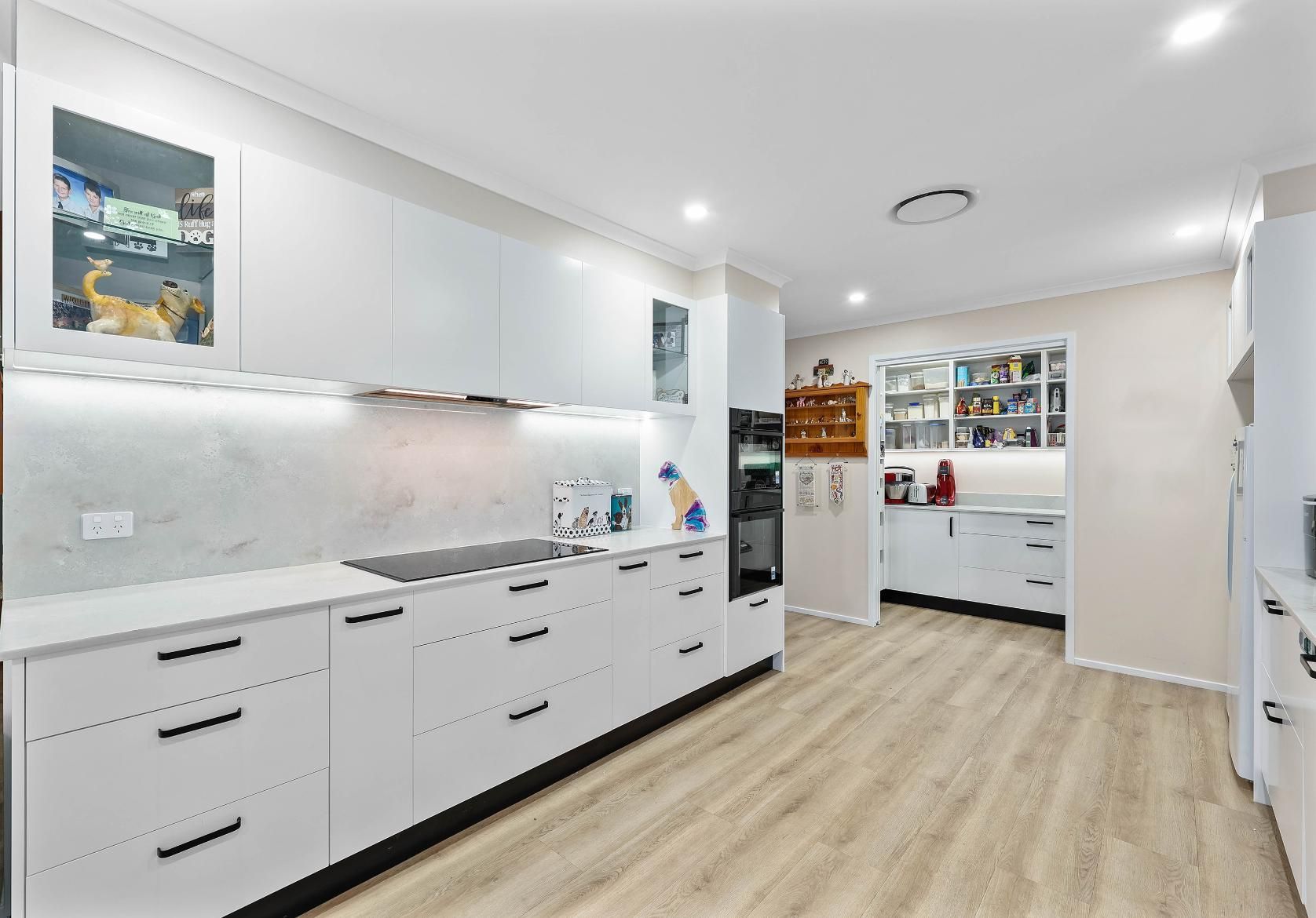 Modern White Kitchen with Black Accents and Light Wood-Look Flooring — Above & Beyond Interiors Custom Joinery in Bradbury, NSW