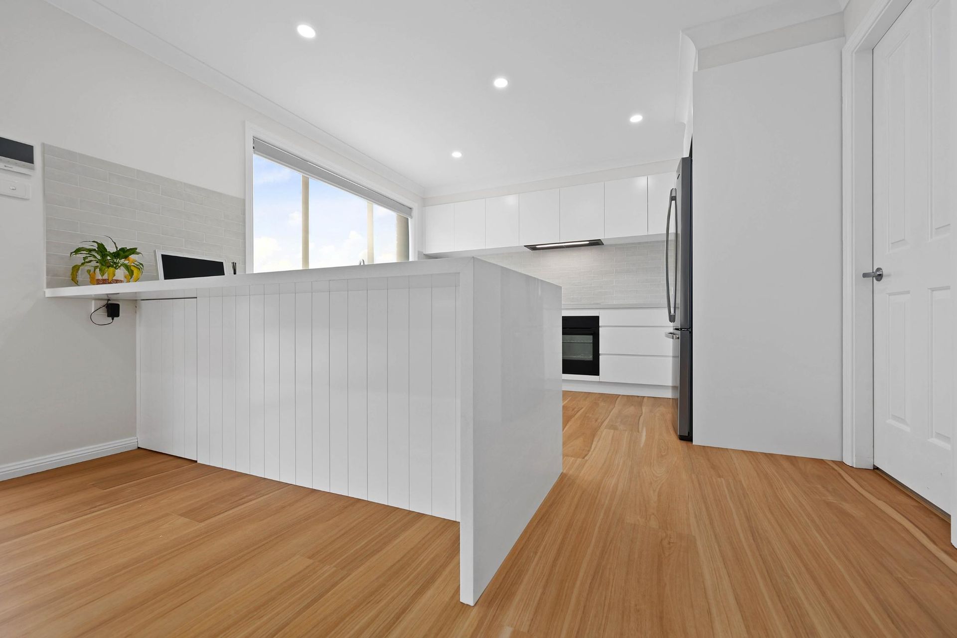 Modern White Kitchen with Wooden Floors, Island, Cabinets, and Appliances — Above & Beyond Interiors Custom Joinery in Mount Anna, NSW
