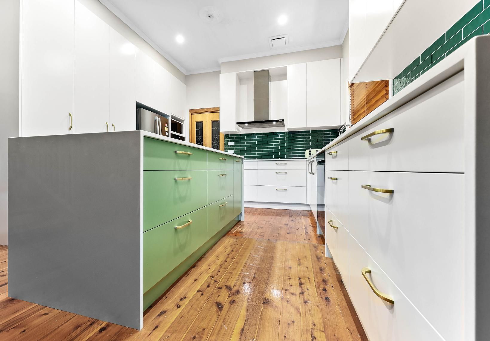 Kitchen with Light Green Island, White Cabinets, Wooden Floor, and Green Backsplash — Above & Beyond Interiors Custom Joinery in Minto, NSW