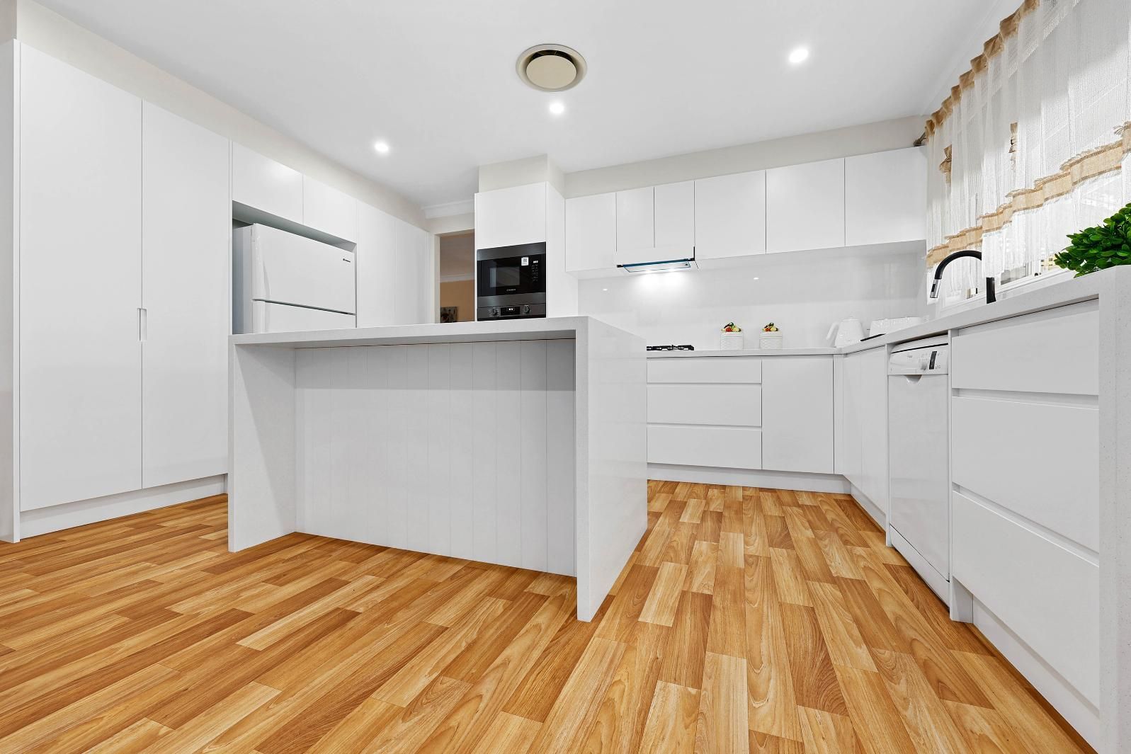 White Modern Kitchen with Wood Flooring; Island, Cabinets, Oven, and Refrigerator Are Visible — Above & Beyond Interiors Custom Joinery in Narellan Vale, NSW