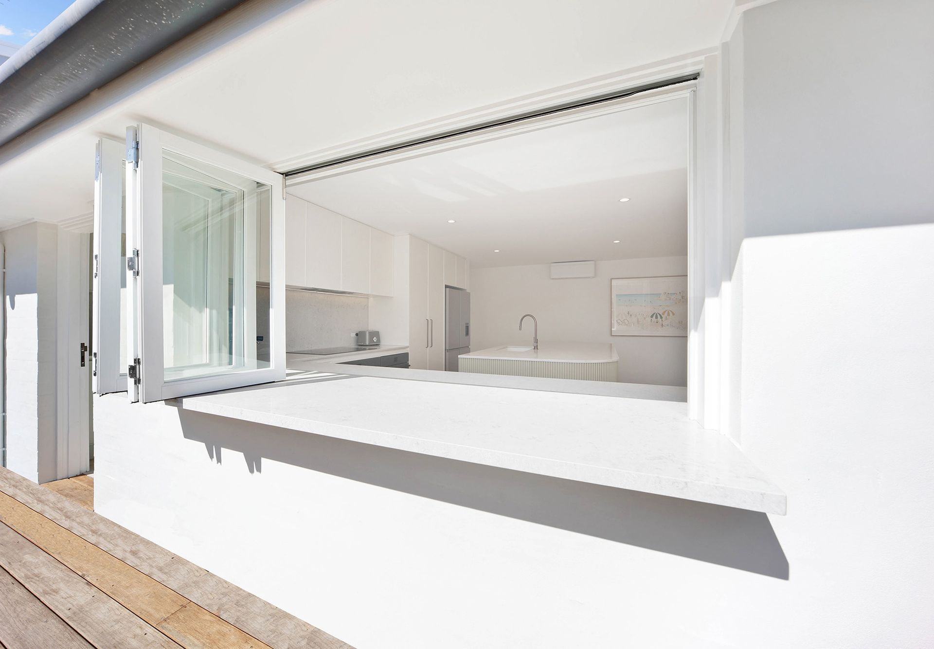 White kitchen with open bi-fold windows, revealing a minimalist interior — Above & Beyond Interiors Custom Joinery in Bellambi, NSW