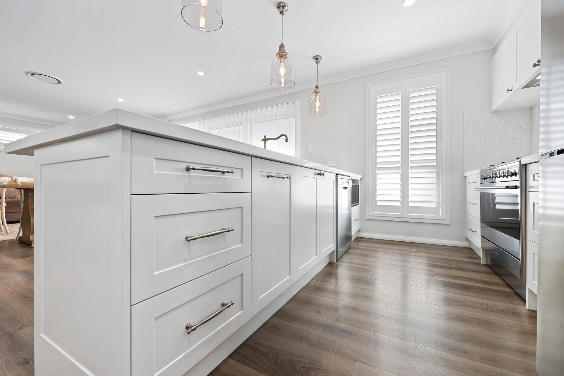 White Kitchen with Island, Stainless Steel Appliances, Wood Floor, and Light Fixtures — Above & Beyond Interiors Custom Joinery in Thirlmere, NSW