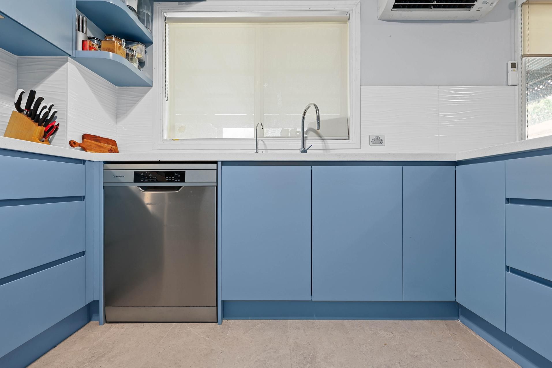 Blue Kitchen with A Dishwasher, Cabinets, White Backsplash, and A Window with A Light-Colored Blind — Above & Beyond Interiors Custom Joinery in Macquarie Fields, NSW