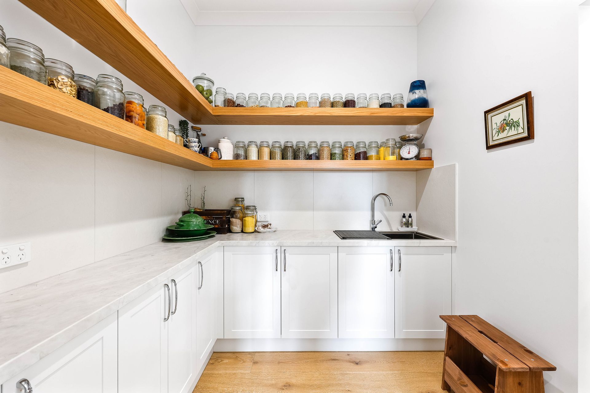 Bright white pantry with wooden shelves filled with jars, sink, and white cabinets — Above & Beyond Interiors Custom Joinery in Bradbury, NSW