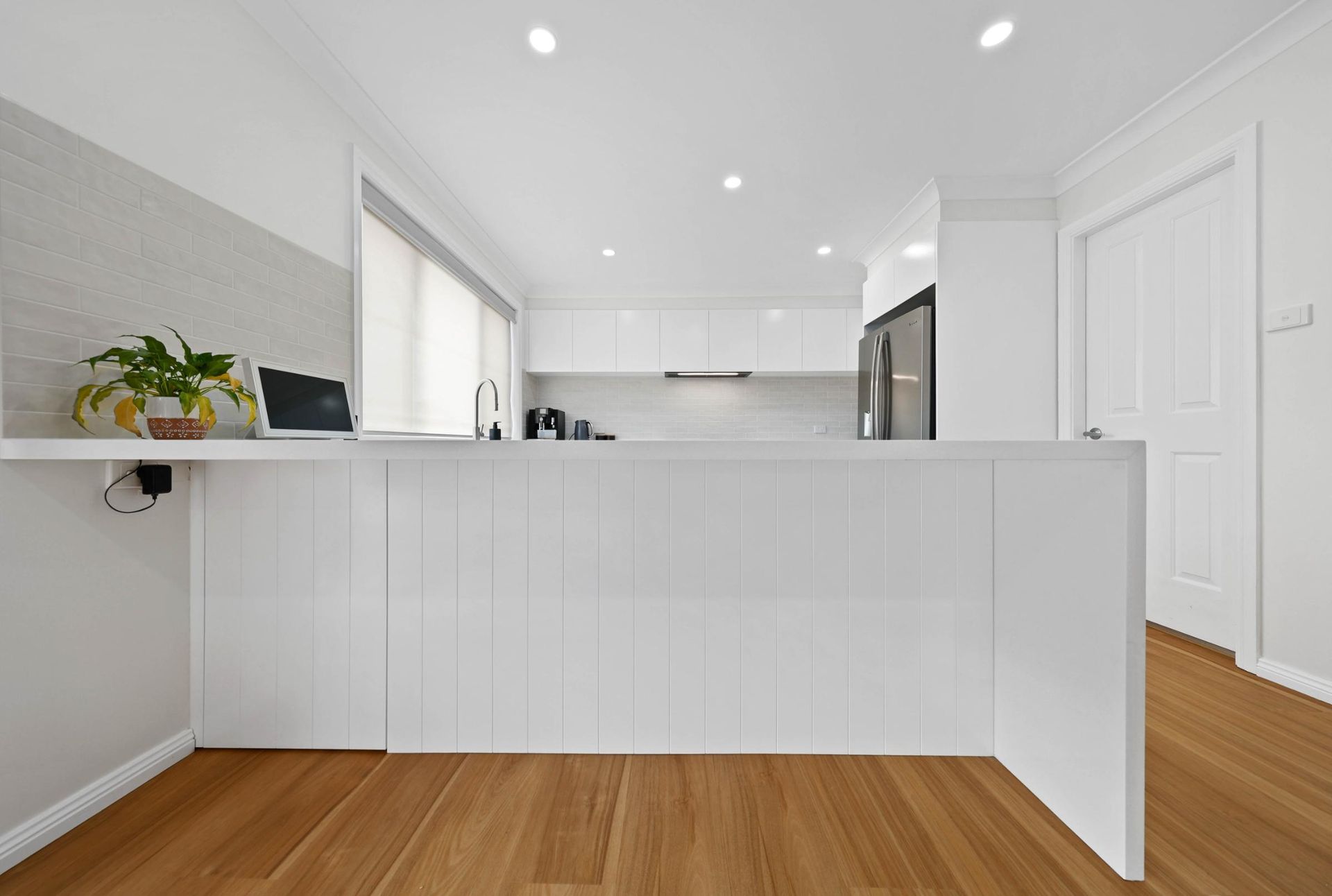 White Kitchen with A Countertop and Wood Floors — Above & Beyond Interiors Custom Joinery in Mount Anna, NSW
