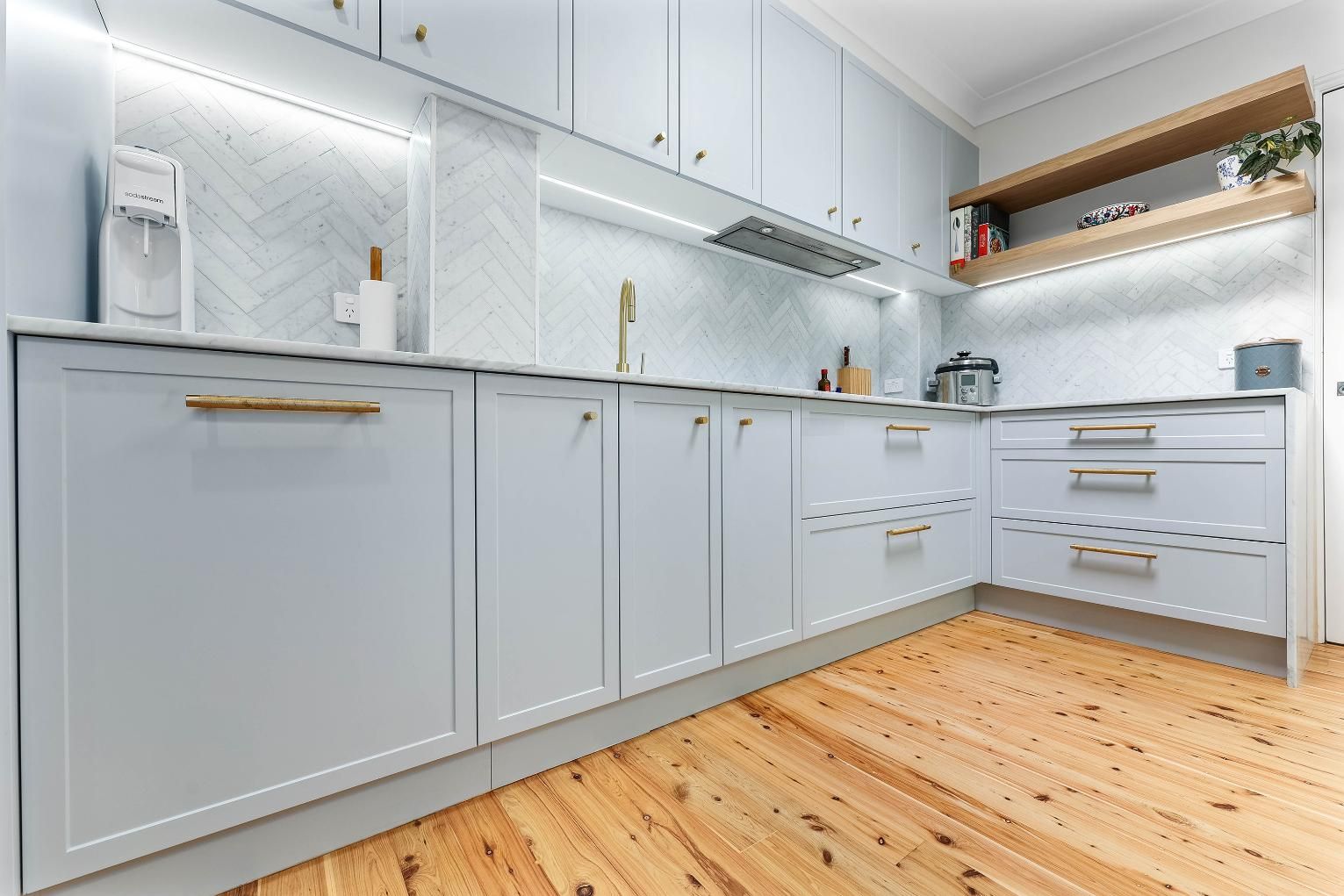 Light Blue Kitchen Cabinets with Gold Hardware, Herringbone Tile Backsplash, and Wooden Floors — Above & Beyond Interiors Custom Joinery in Erskineville, NSW