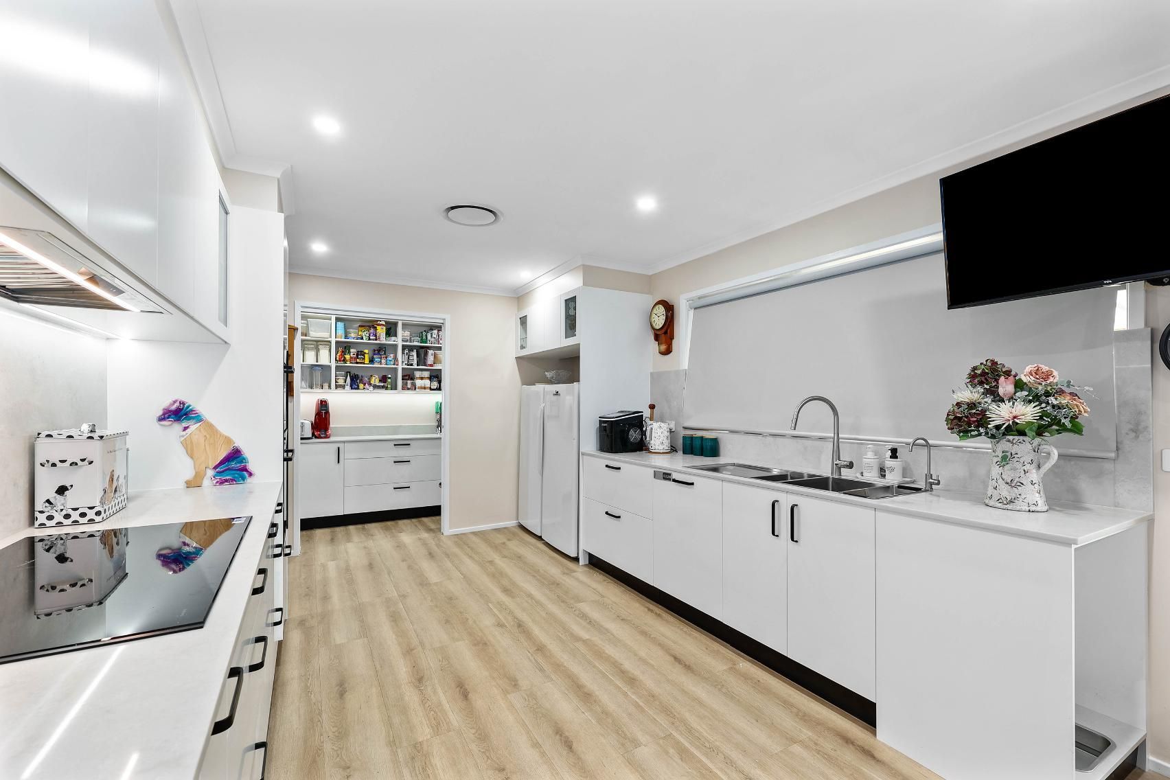 Bright White Kitchen with Light Wood Flooring, Stainless Steel Appliances, and A Large Tv — Above & Beyond Interiors Custom Joinery in Bradbury, NSW