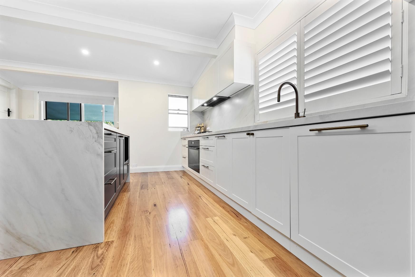 Modern Kitchen with White Cabinets, Marble Island, Wooden Floors, and Shuttered Window — Above & Beyond Interiors Custom Joinery in Bellambi, NSW