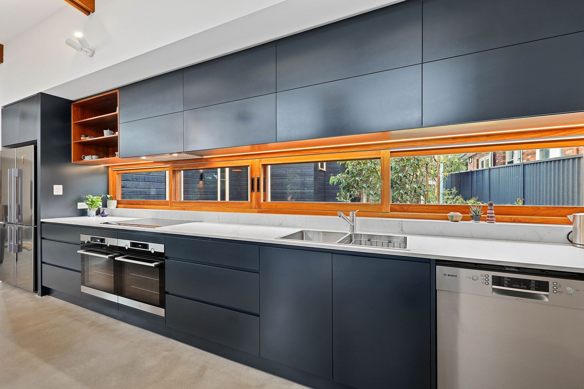 Modern kitchen with dark blue cabinets, wooden accents, and a stainless steel refrigerator — Above & Beyond Interiors Custom Joinery in Bellambi, NSW