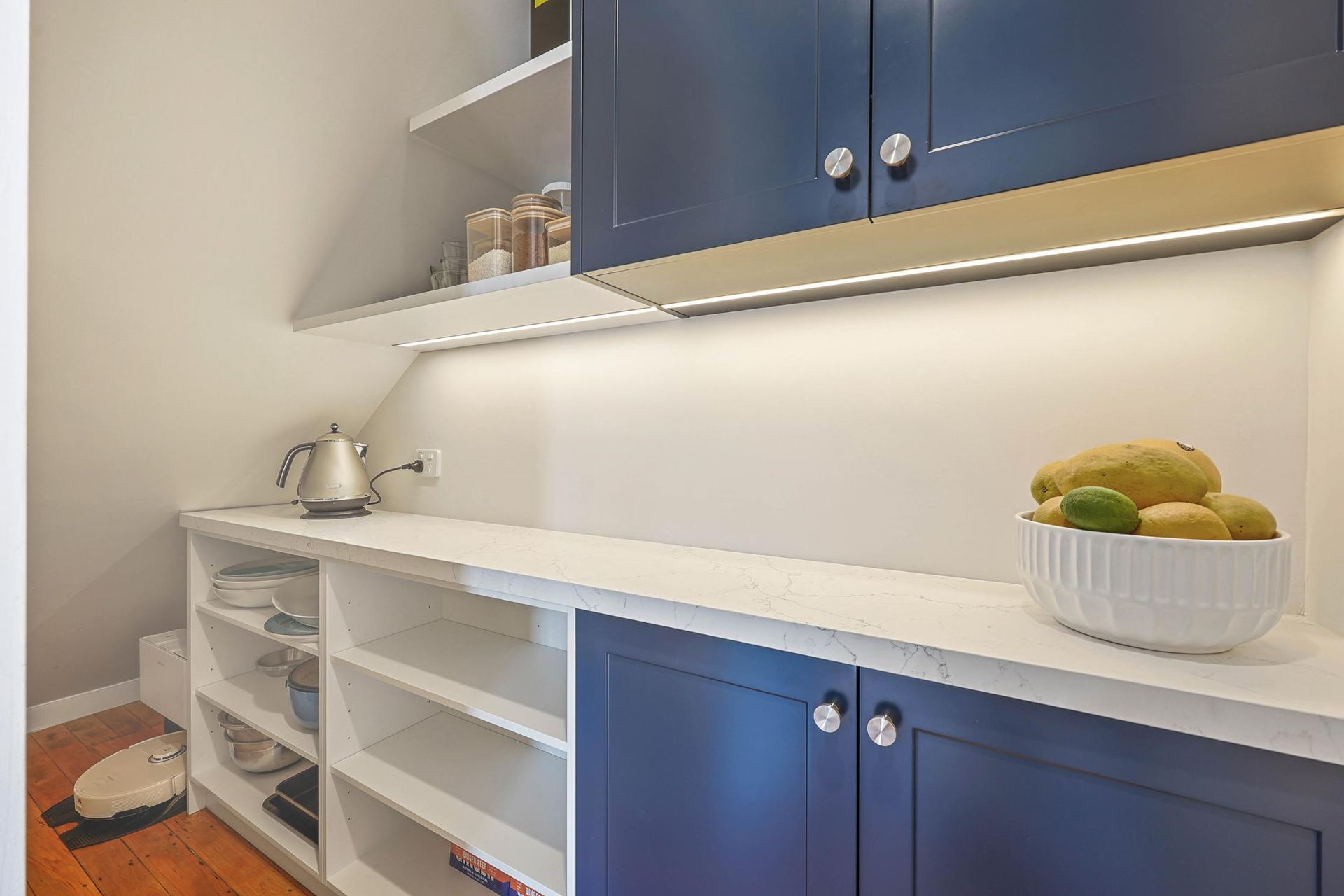 Pantry with White Countertops, Blue Cabinets, and Open Shelving; a Bowl of Fruit Sits on The Counter — Above & Beyond Interiors Custom Joinery in Lilyfield, NSW