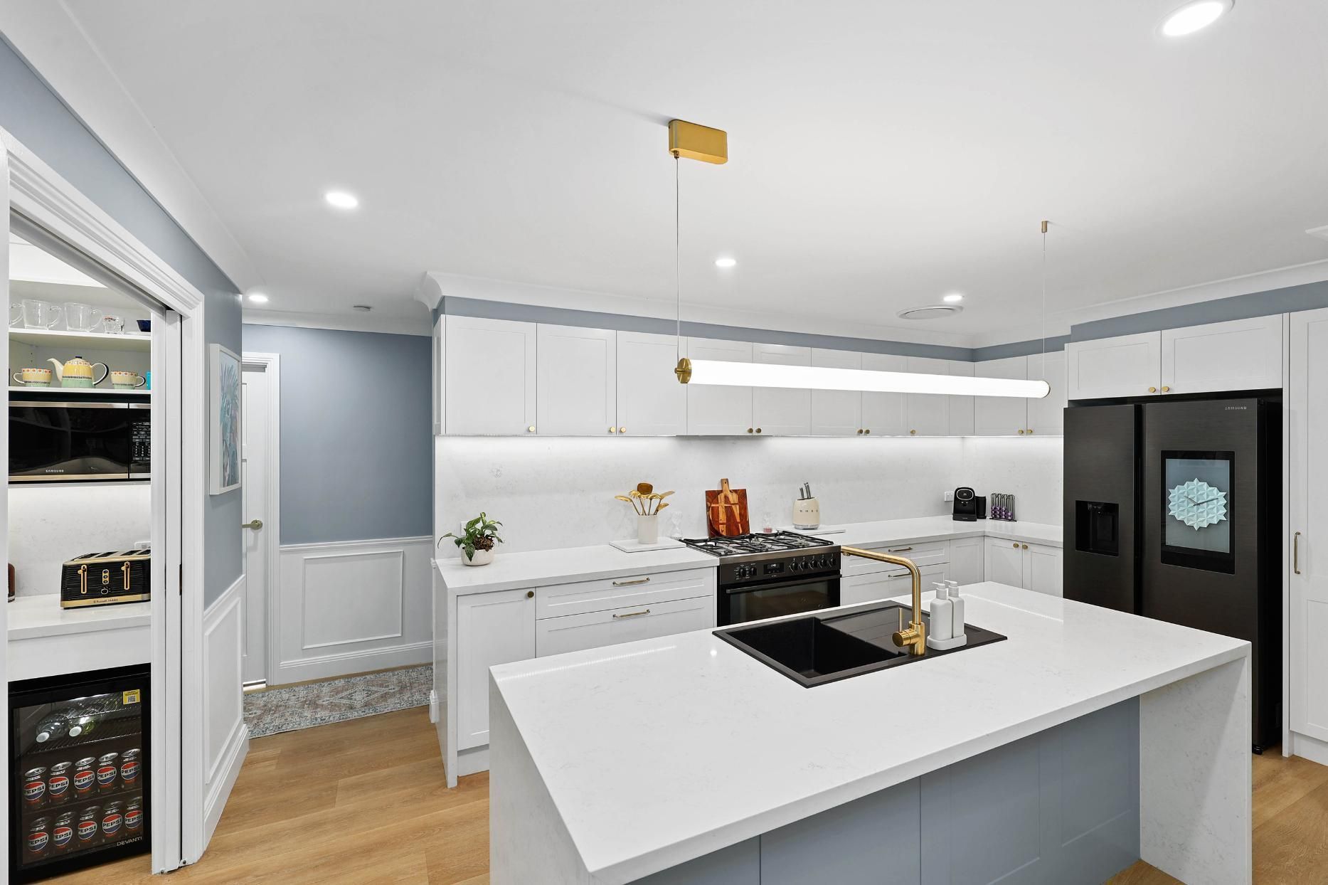 Modern Kitchen with White Cabinets, Large Island, Black Appliances, and Pantry on The Left — Above & Beyond Interiors Custom Joinery in Harrington Park, NSW