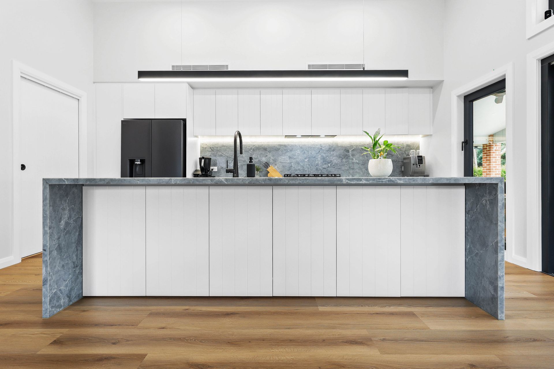 Modern white kitchen with island, grey countertop, black refrigerator, and wooden floor — Above & Beyond Interiors Custom Joinery in Bellambi, NSW
