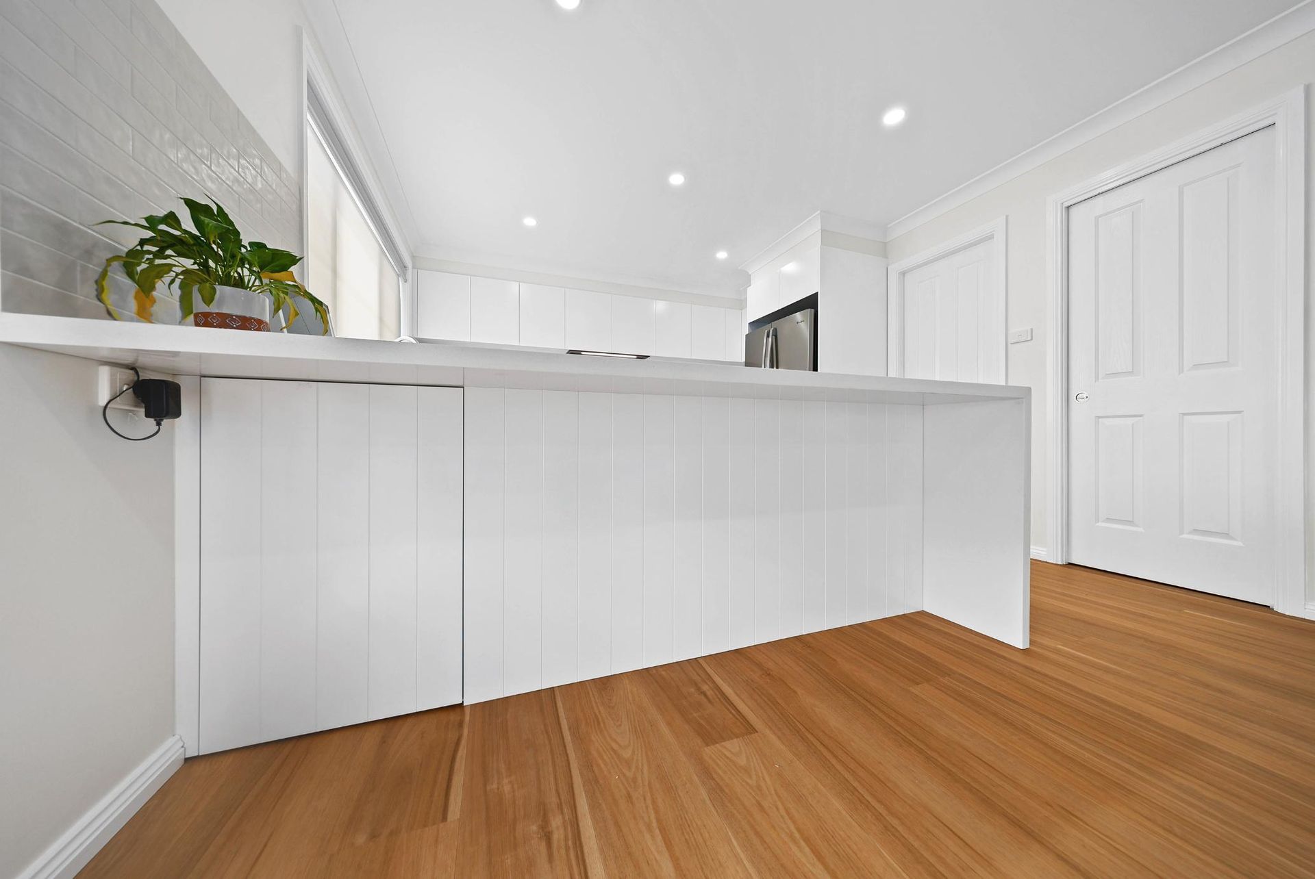 White Kitchen Island with Wood Floor, Window, Doors, and Overhead Lighting — Above & Beyond Interiors Custom Joinery in Mount Anna, NSW