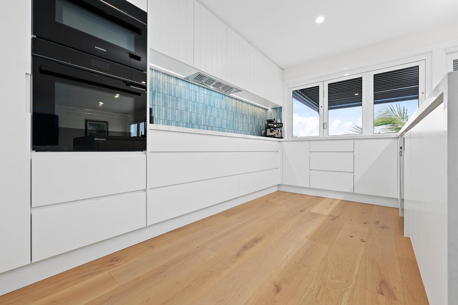 Modern White Kitchen with Wood Floors, Black Oven, and Window — Above & Beyond Interiors Custom Joinery in North Curl Curl, NSW