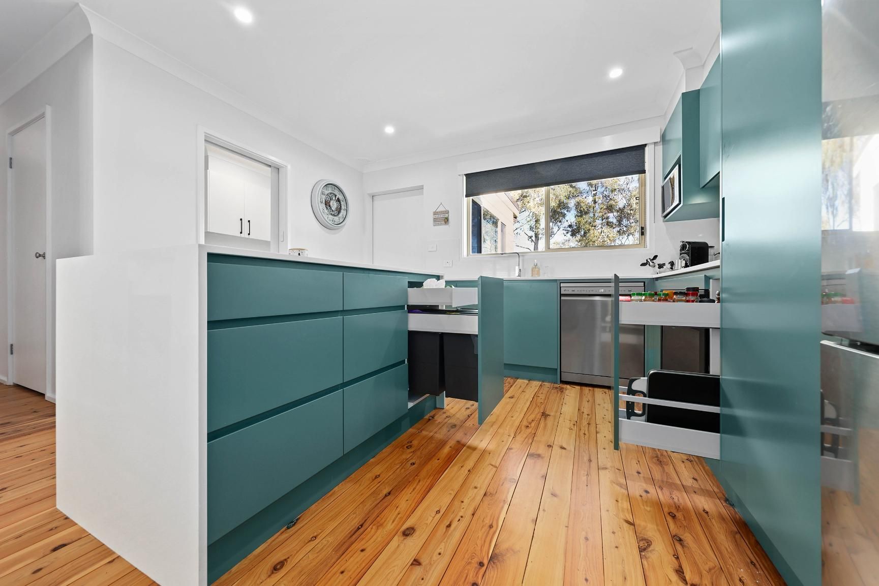 Teal Kitchen with White Accents, Wooden Floor, Open Drawers, and A View of A Window and Trees — Above & Beyond Interiors Custom Joinery in Bradbury, NSW