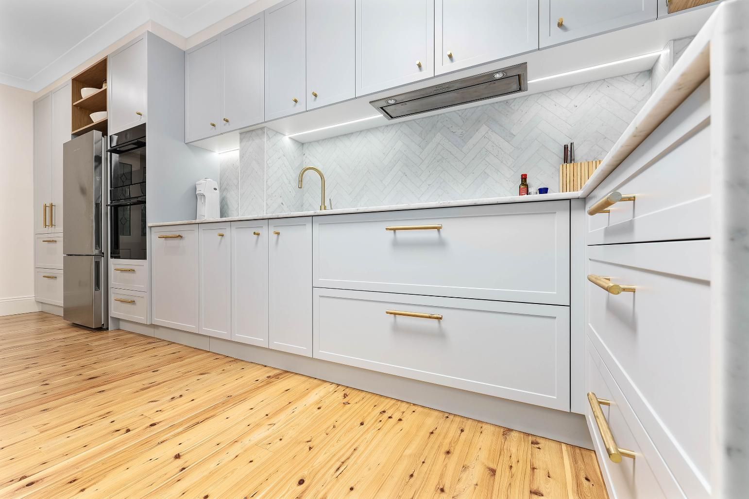 Light Blue and White Kitchen with Gold Hardware, Light Wood Floor, and White Backsplash — Above & Beyond Interiors Custom Joinery in Erskineville, NSW