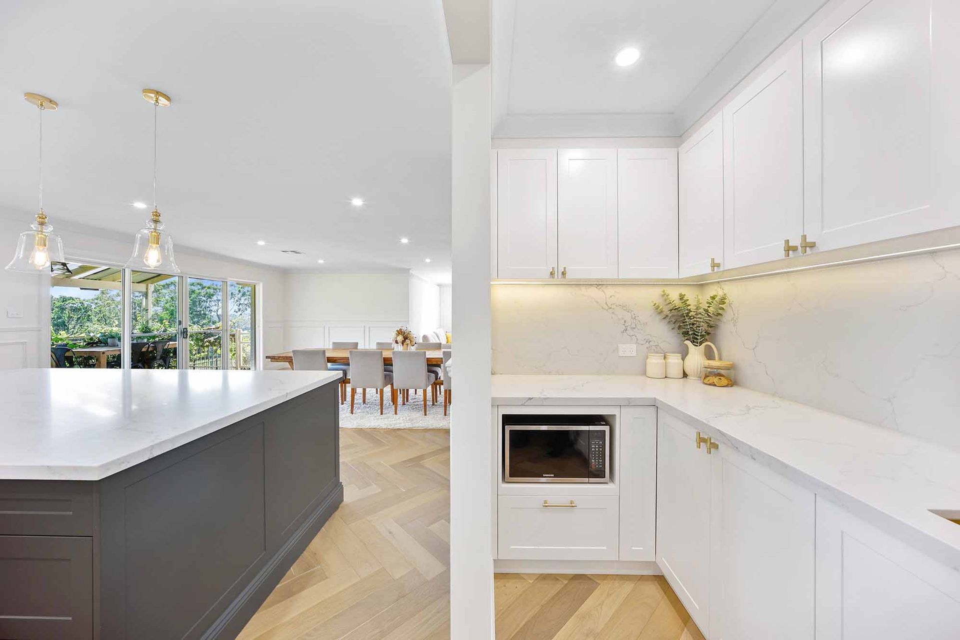 Kitchen with white cabinets, a grey island, and a dining room visible in the background — Above & Beyond Interiors Custom Joinery in Bellambi, NSW