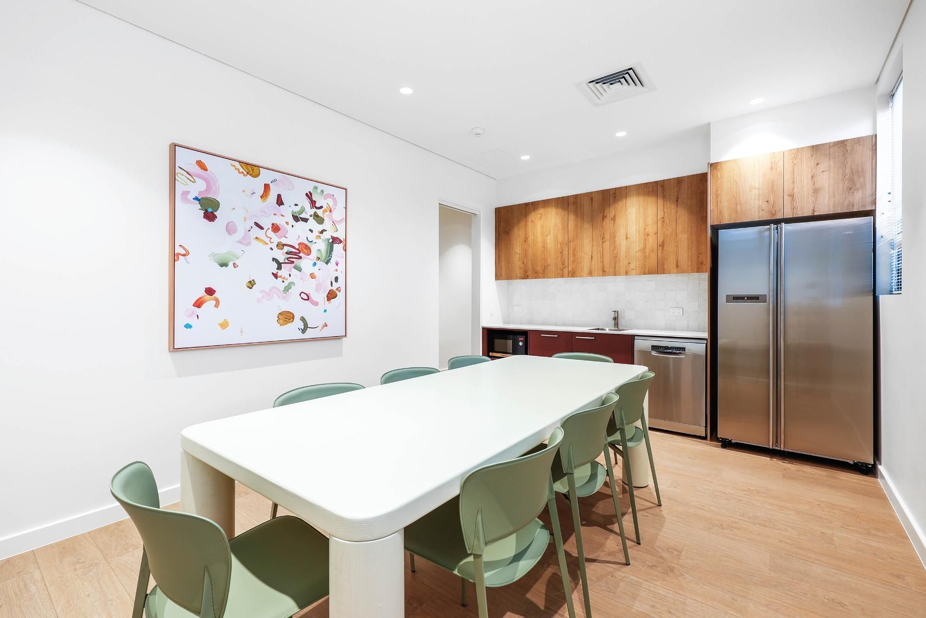Conference Room with White Table and Green Chairs. Kitchen Area with Wood Cabinets and Stainless Steel Fridge — Above & Beyond Interiors Custom Joinery in Medical Centre, NSW