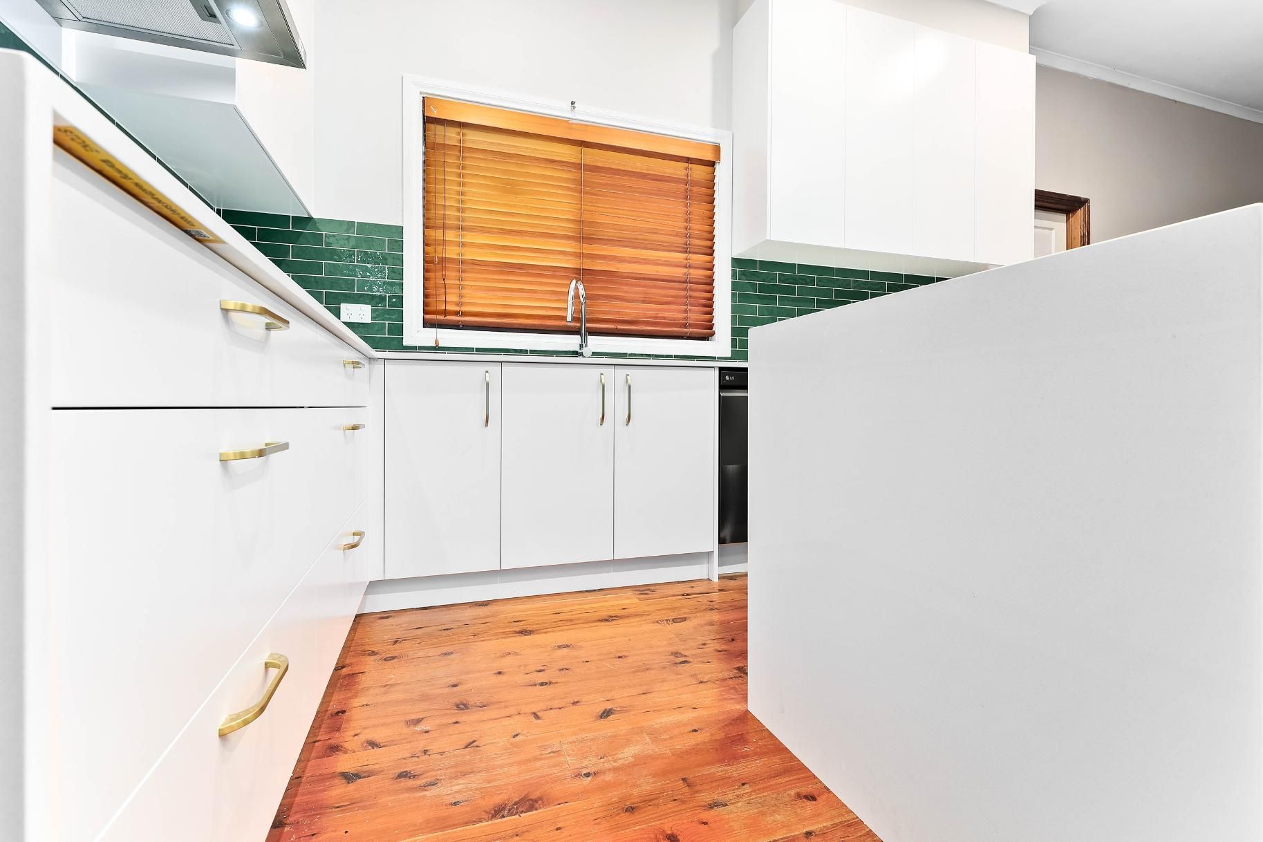 White Kitchen with Wooden Floor, White Cabinets, Green Tiled Backsplash, and A Brown Window Shade — Above & Beyond Interiors Custom Joinery in Minto, NSW