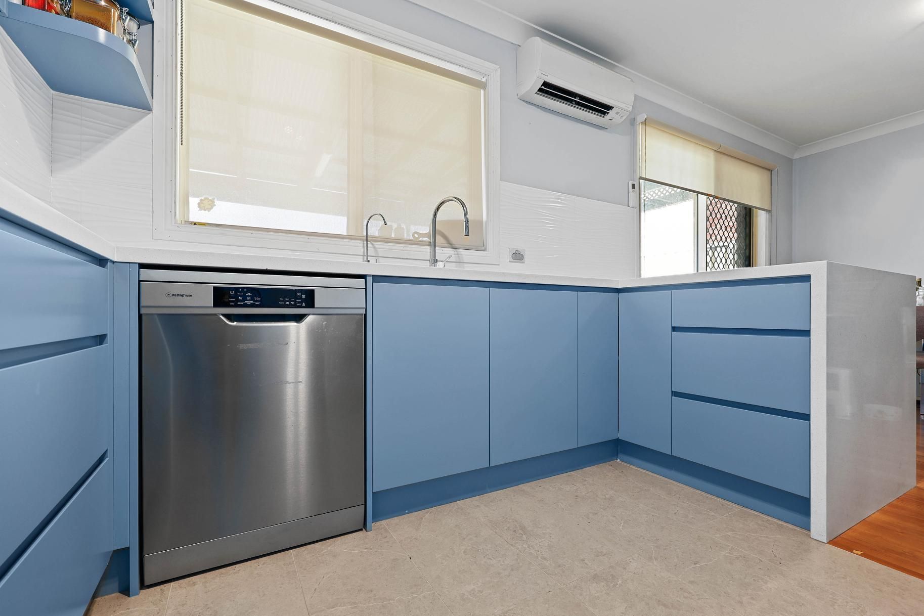 Modern Kitchen with Light Blue Cabinets, Stainless Steel Dishwasher, and A Window with Blinds — Above & Beyond Interiors Custom Joinery in Macquarie Fields, NSW