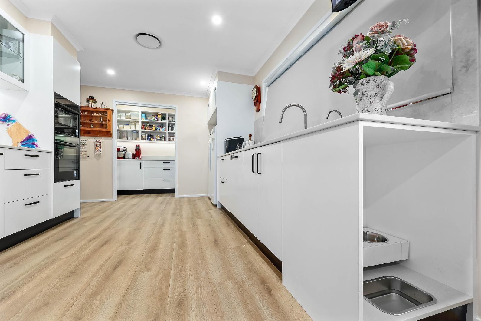 Bright White Kitchen with Light Wood Floors, Built-In Appliances, and A Stainless Steel Sink — Above & Beyond Interiors Custom Joinery in Bradbury, NSW