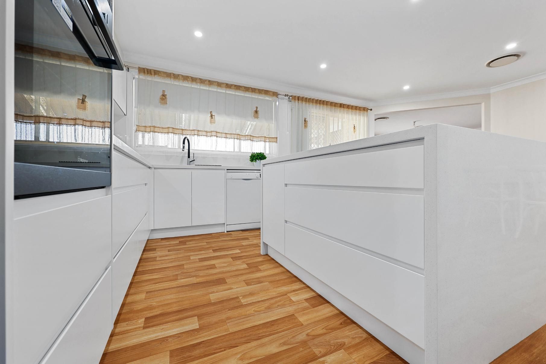 Modern White Kitchen with Island, Wooden Floors, and Natural Light — Above & Beyond Interiors Custom Joinery in Narellan Vale, NSW