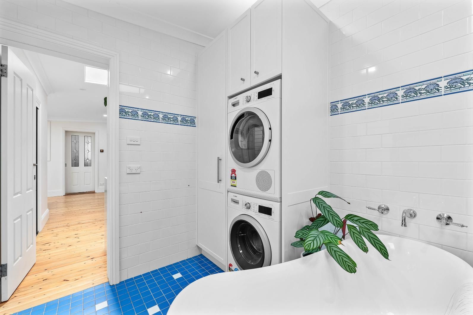 Laundry Room with Stacked Washer/dryer, Blue Tile Floor, White Walls, and Bathtub — Above & Beyond Interiors Custom Joinery in Erskineville, NSW