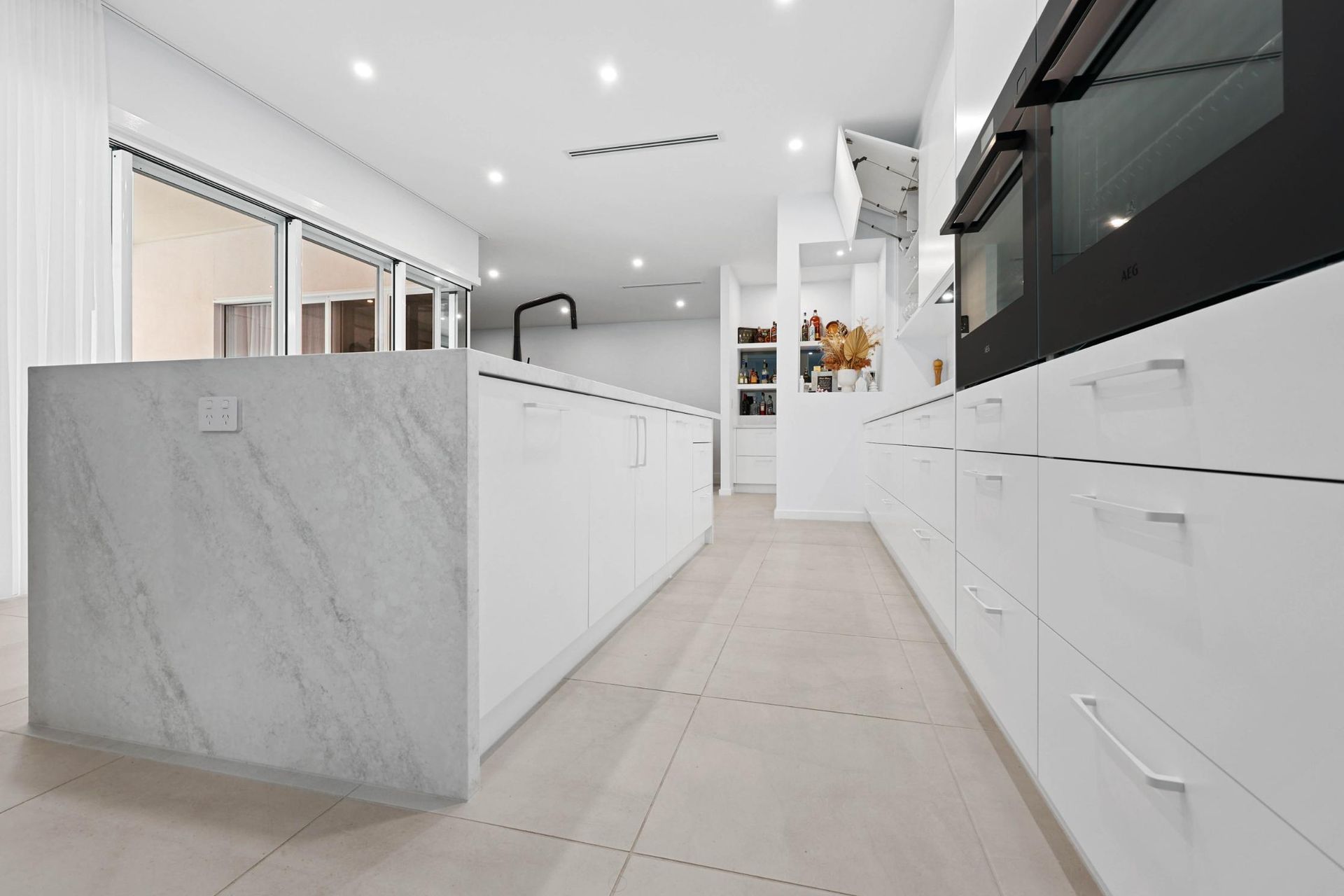 Modern, Bright White Kitchen with Marble Island, Oven, Cabinets, and Large Windows — Above & Beyond Interiors Custom Joinery in Currans Hill, NSW