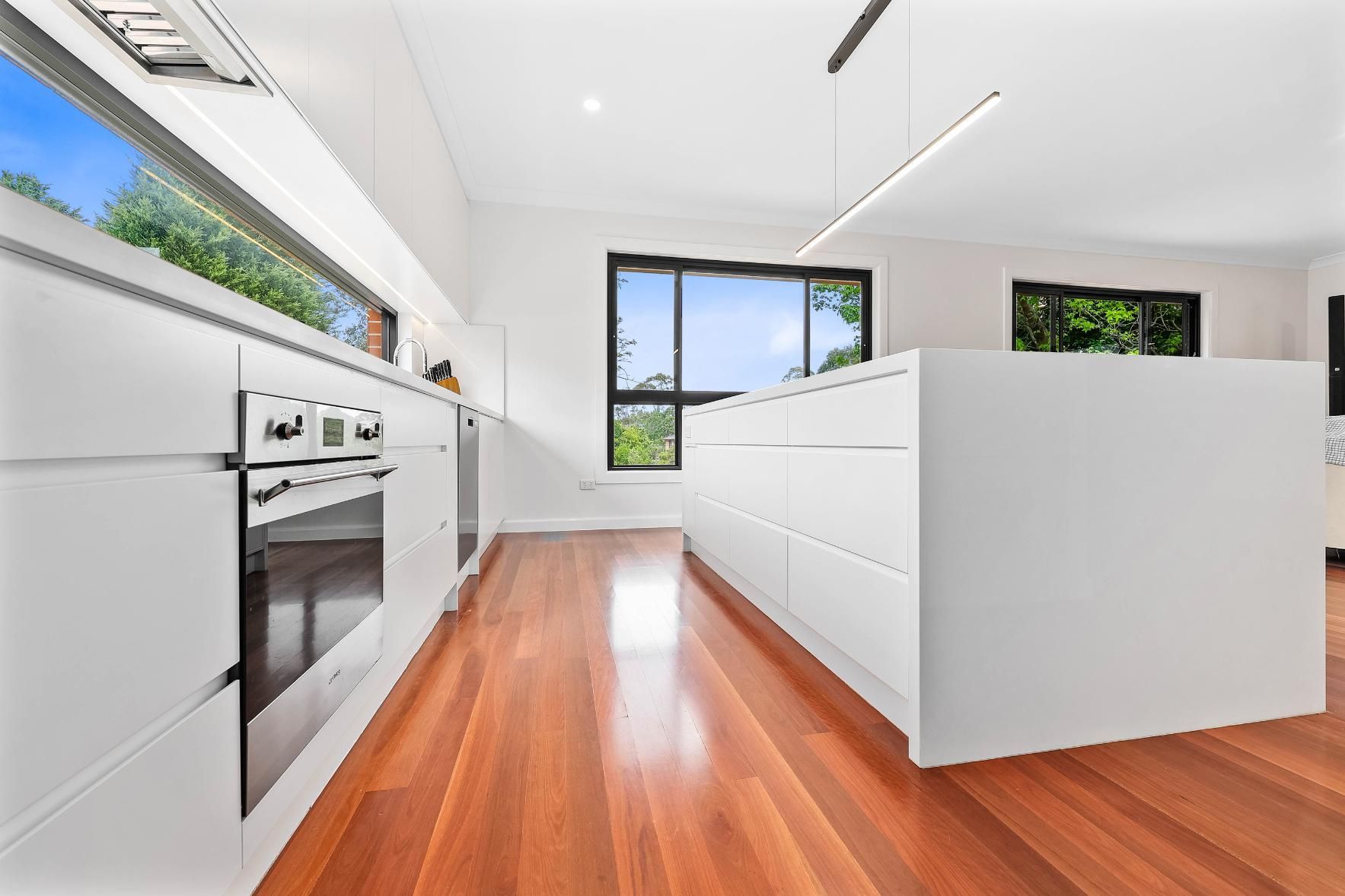 Modern White Kitchen with Wooden Floors, Island, and Large Windows — Above & Beyond Interiors Custom Joinery in Killara, NSW