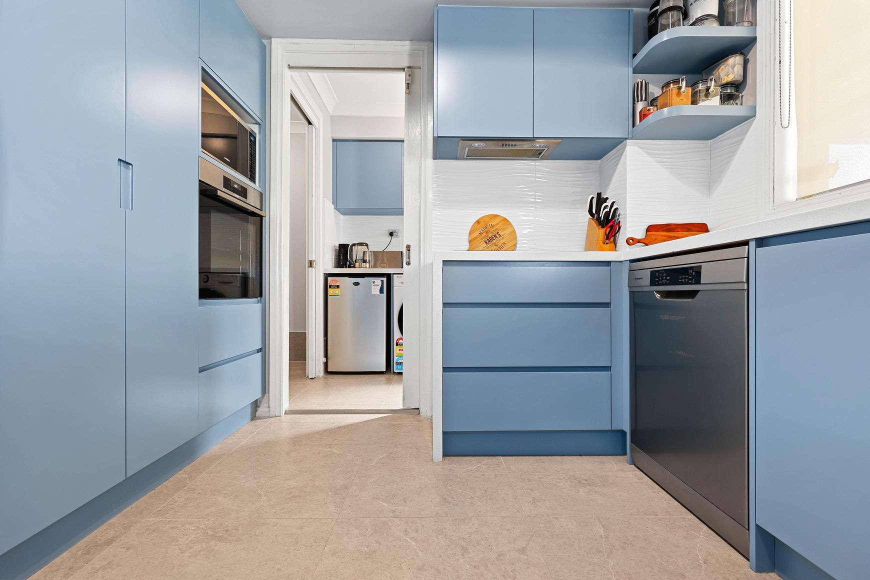 Blue Kitchen with Oven, Cabinetry, and Dishwasher; Leads to A Hallway with Appliances — Above & Beyond Interiors Custom Joinery in Macquarie Fields, NSW