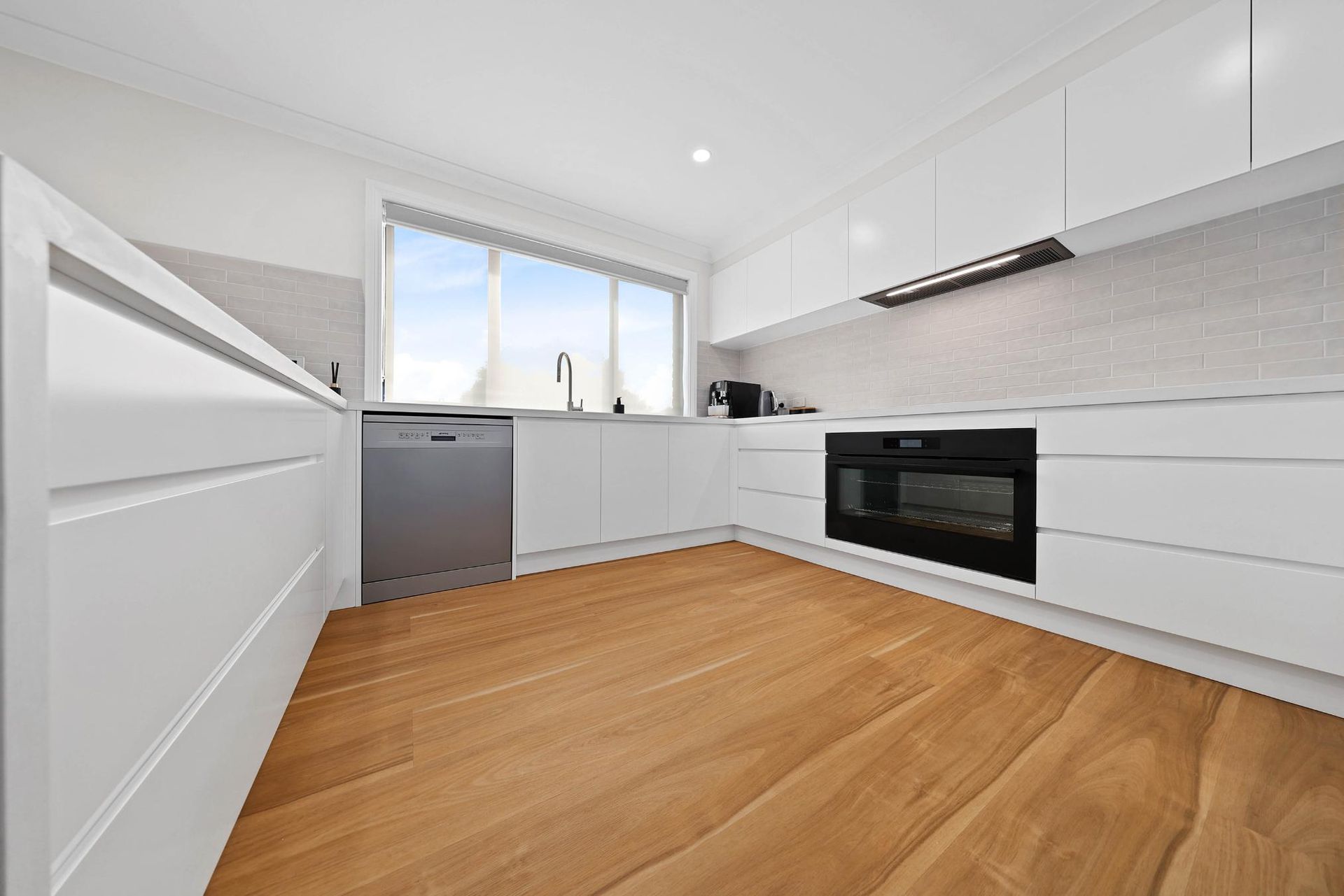 White Modern Kitchen with Wooden Floors, Dishwasher, and Oven — Above & Beyond Interiors Custom Joinery in Mount Anna, NSW