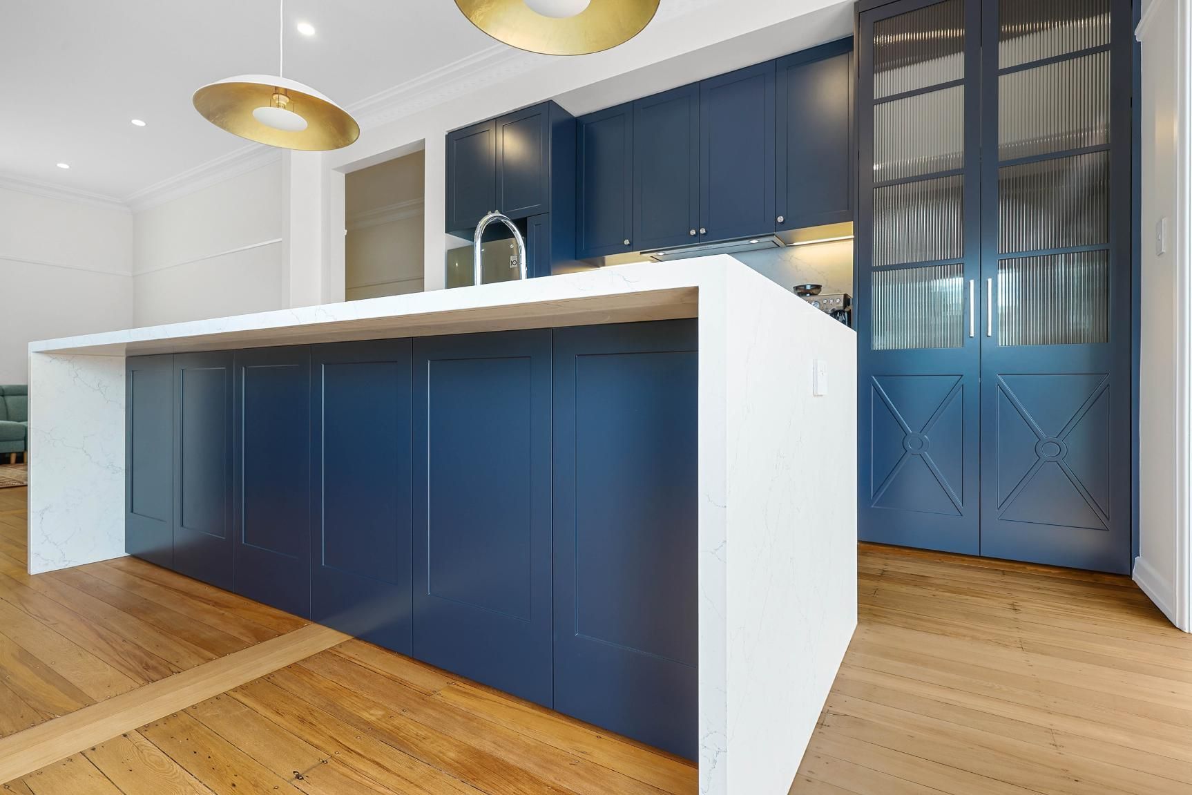 Modern Kitchen with White Island and Navy Blue Cabinets, Gold Lights, and Wooden Floor — Above & Beyond Interiors Custom Joinery in Lilyfield, NSW
