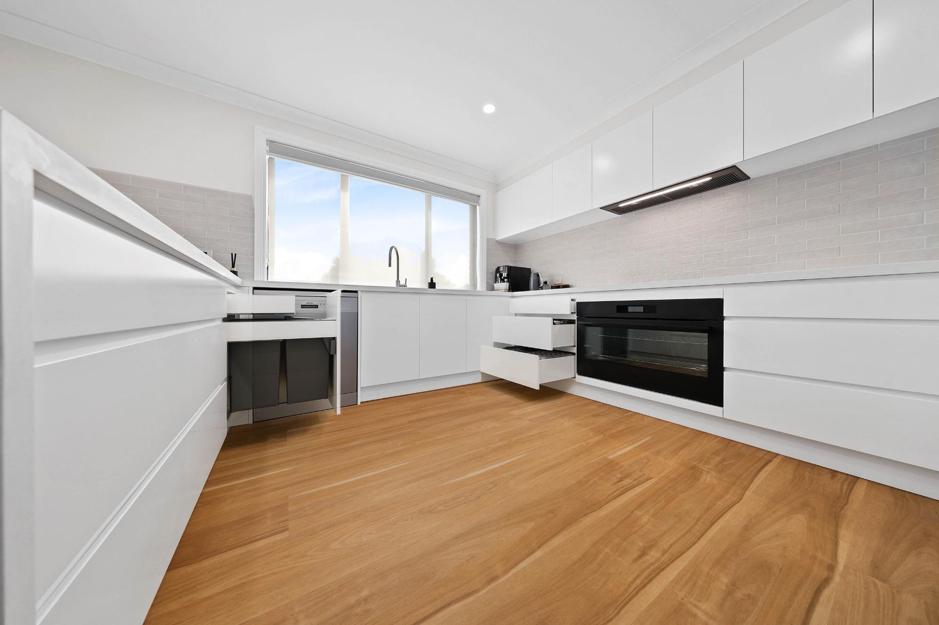 Modern, All-White Kitchen with Wood Floors. Cabinets, Oven, and A Window Are Visible — Above & Beyond Interiors Custom Joinery in Mount Anna, NSW
