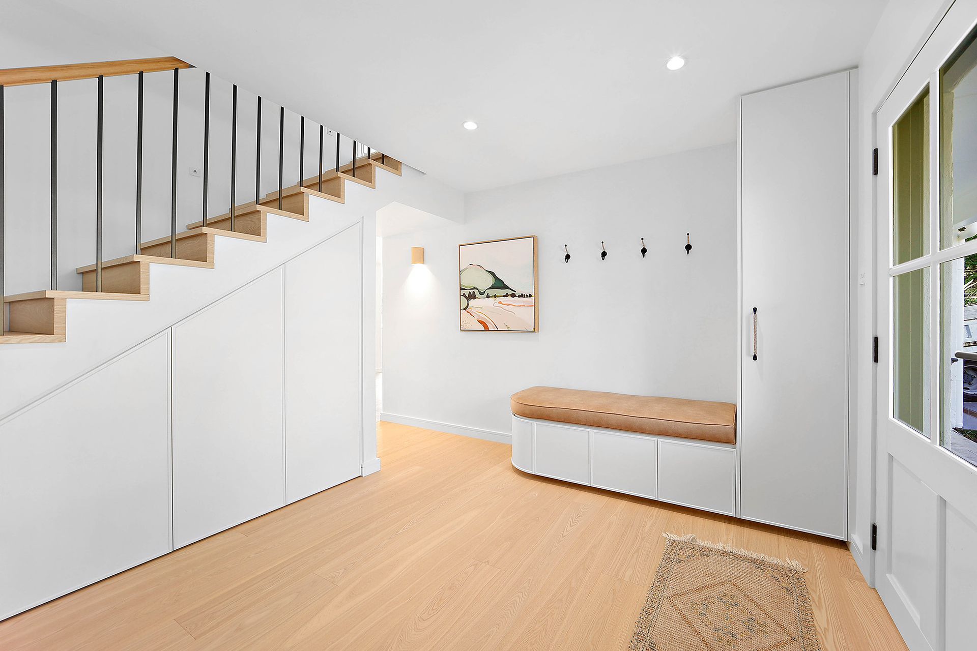 Bright entry hall with stairs, storage, and bench. White walls, wood floor, and neutral art — Above & Beyond Interiors Custom Joinery in Bellambi, NSW