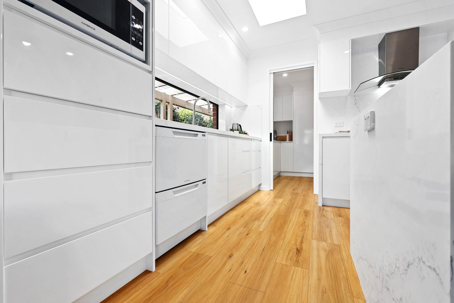 Modern White Kitchen with Wood Floors and A Skylight — Above & Beyond Interiors Custom Joinery in Wattle Grove, NSW